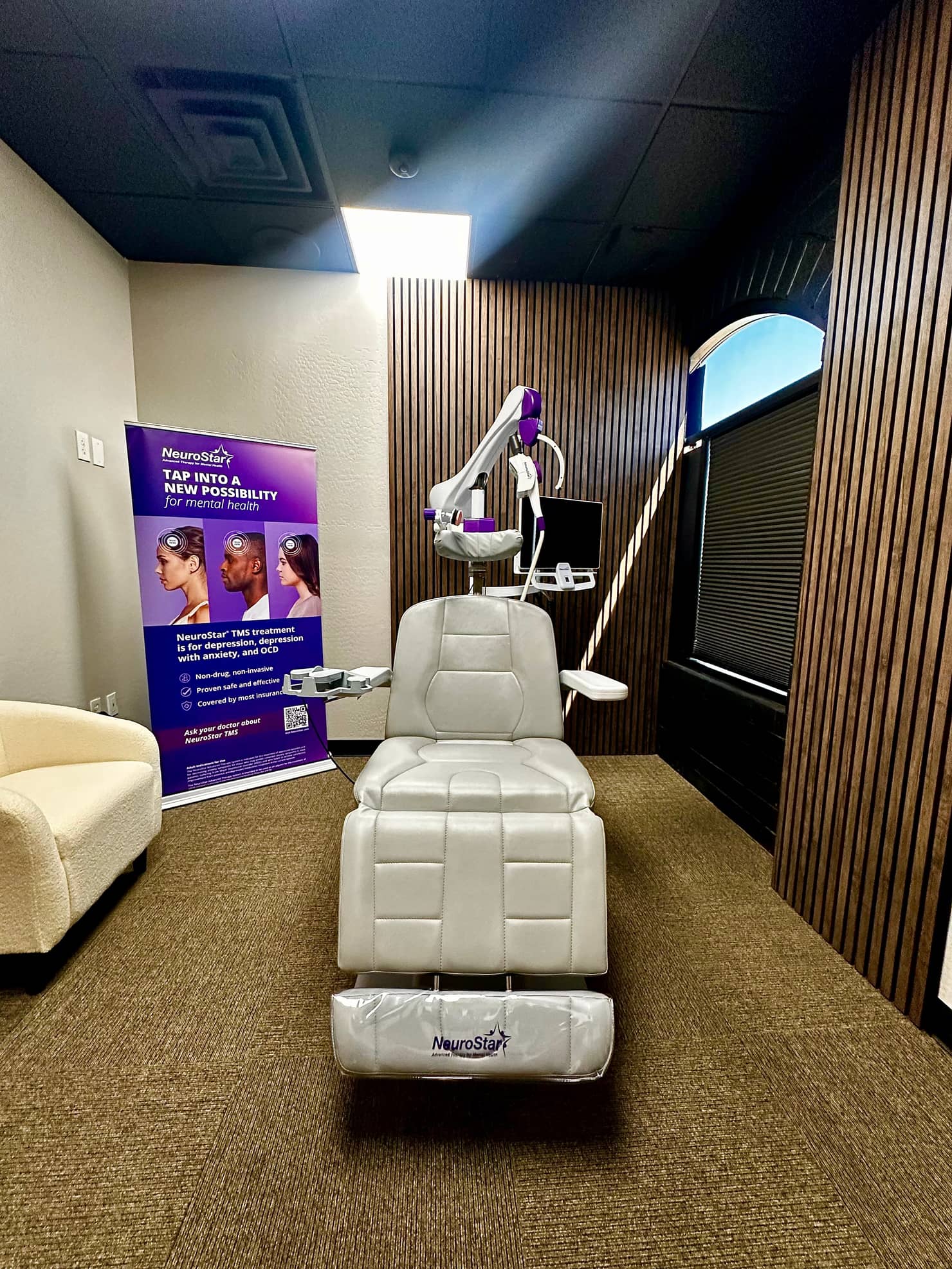 The NeuroStar treatment chair facing forward in the Desert TMS treatment room, with the coil arm overhead.