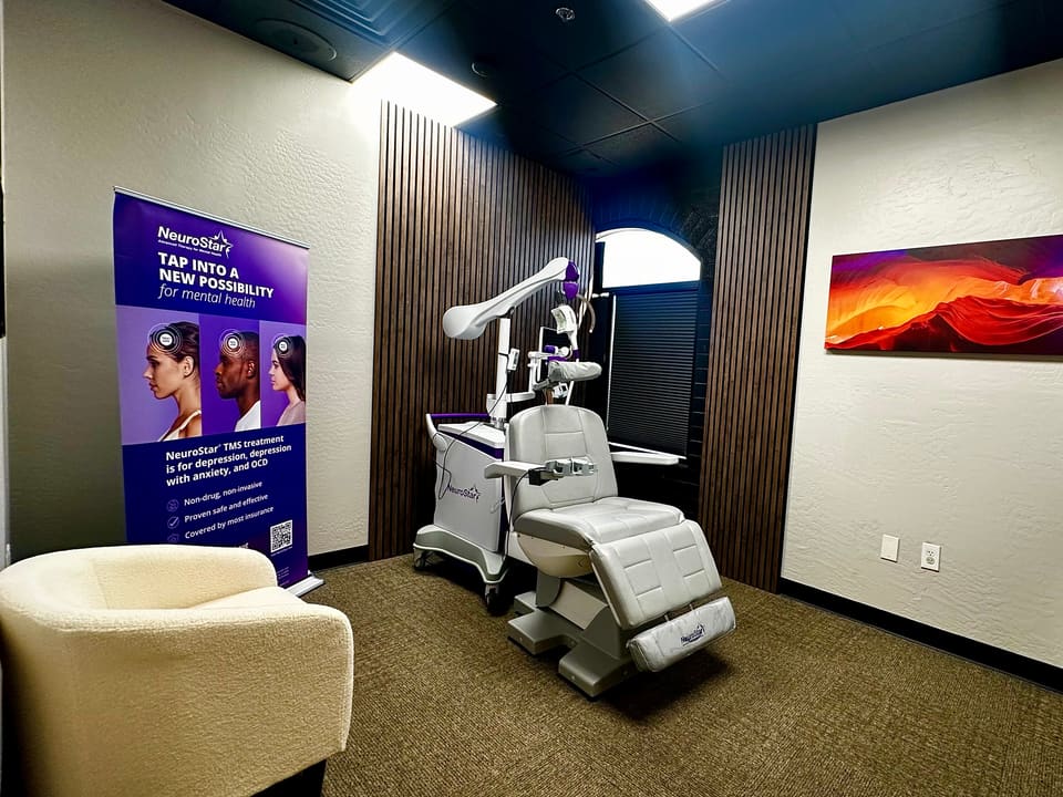 The Desert TMS treatment room: NeuroStar treatment chair in the center, an armchair, and an informational banner.